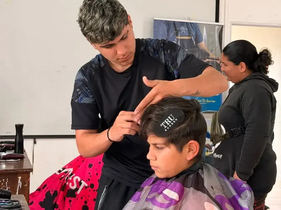 Un joven barbero realiza un corte de cabello gratuito a un niño durante la jornada solidaria organizada en el CIC de Iturbide. La iniciativa Tijeras Solidarias busca brindar servicios de peluquería a los vecinos de la comunidad local.