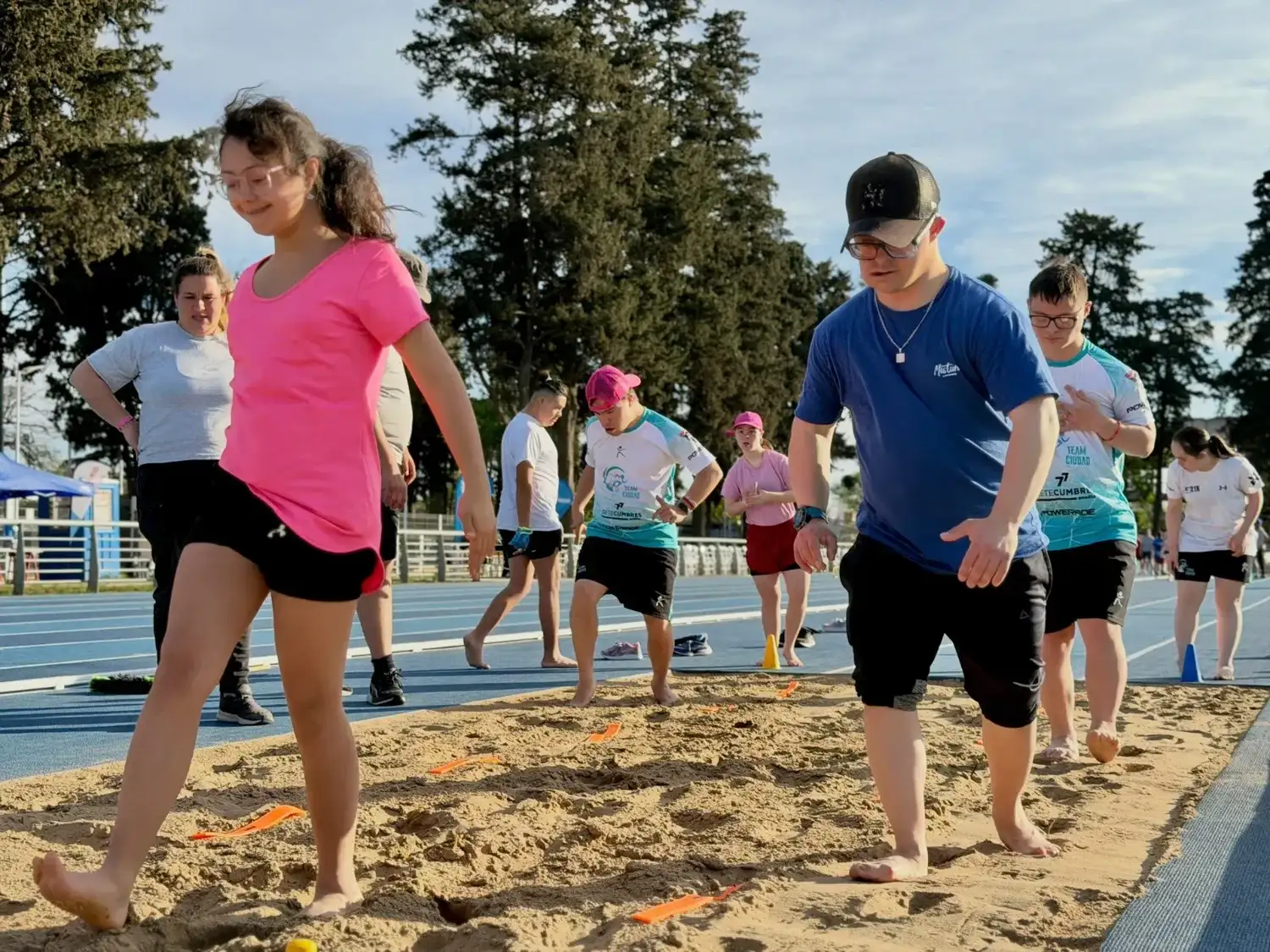 Atletas con Síndrome de Down participan de una jornada de entrenamiento y salto en largo durante el campus abierto realizado en la pista de atletismo de Venado Tuerto, promoviendo la inclusión deportiva y el desarrollo de habilidades físicas.