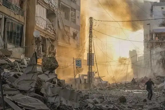 Un hombre corre a ponerse a cubierto mientras de fondo se puede ver el humo provocado por un ataque aéreo israelí en Dahiyeh, Beirut, Líbano, este viernes