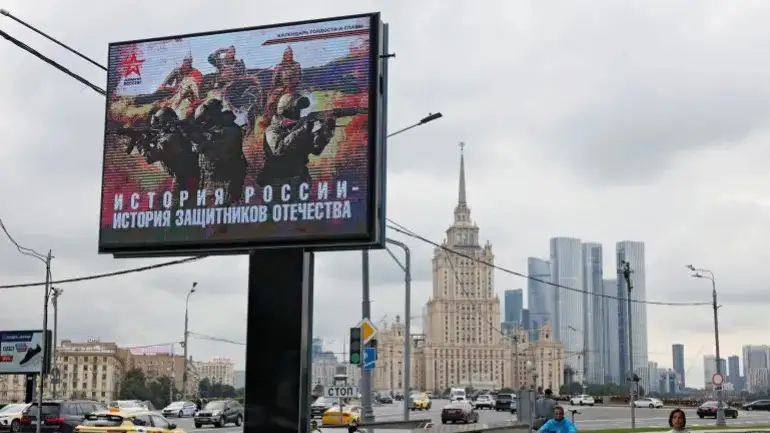 La gente camina junto a una pancarta de apoyo al ejército ruso en Moscú el 11 de agosto de 2025. La pancarta dice: «La historia de Rusia es la historia de los defensores de la patria». [Yulia Morozova/Reuters]
