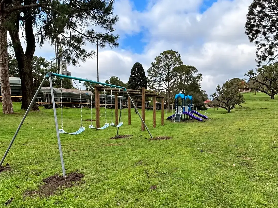 Nuevos juegos infantiles instalados en una plaza de Hughes, incluyendo hamacas y un tobogán, como parte del plan de mejoras en espacios recreativos locales para el disfrute de los niños en un entorno natural al aire libre.
