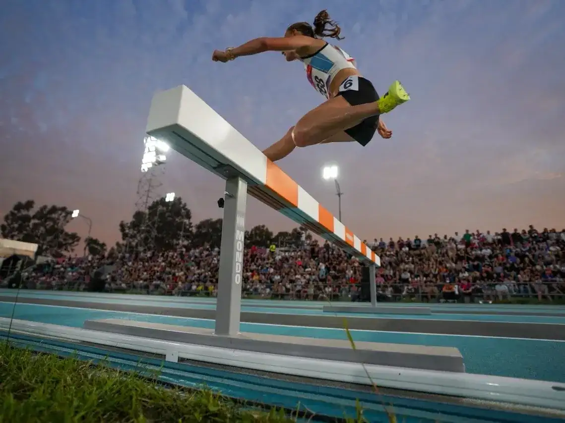 Una atleta salta una valla durante una competencia de atletismo en los Juegos Suramericanos realizados en Santa Fe, evento que dejó un impacto económico millonario y una gran convocatoria de público en las pistas de la ciudad.