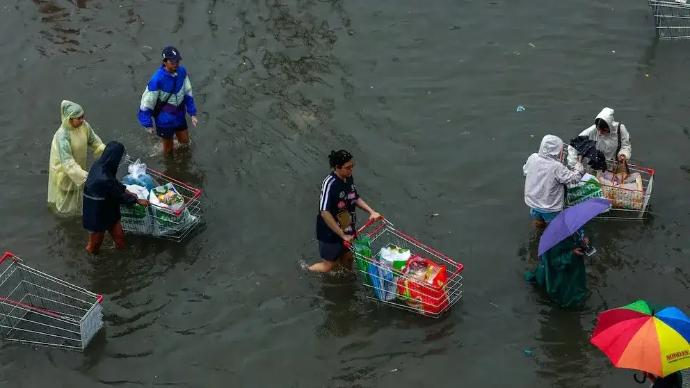 Personas transportan alimentos mientras avanzan por una calle inundada durante fuertes lluvias en Bangkok, Tailandia,
